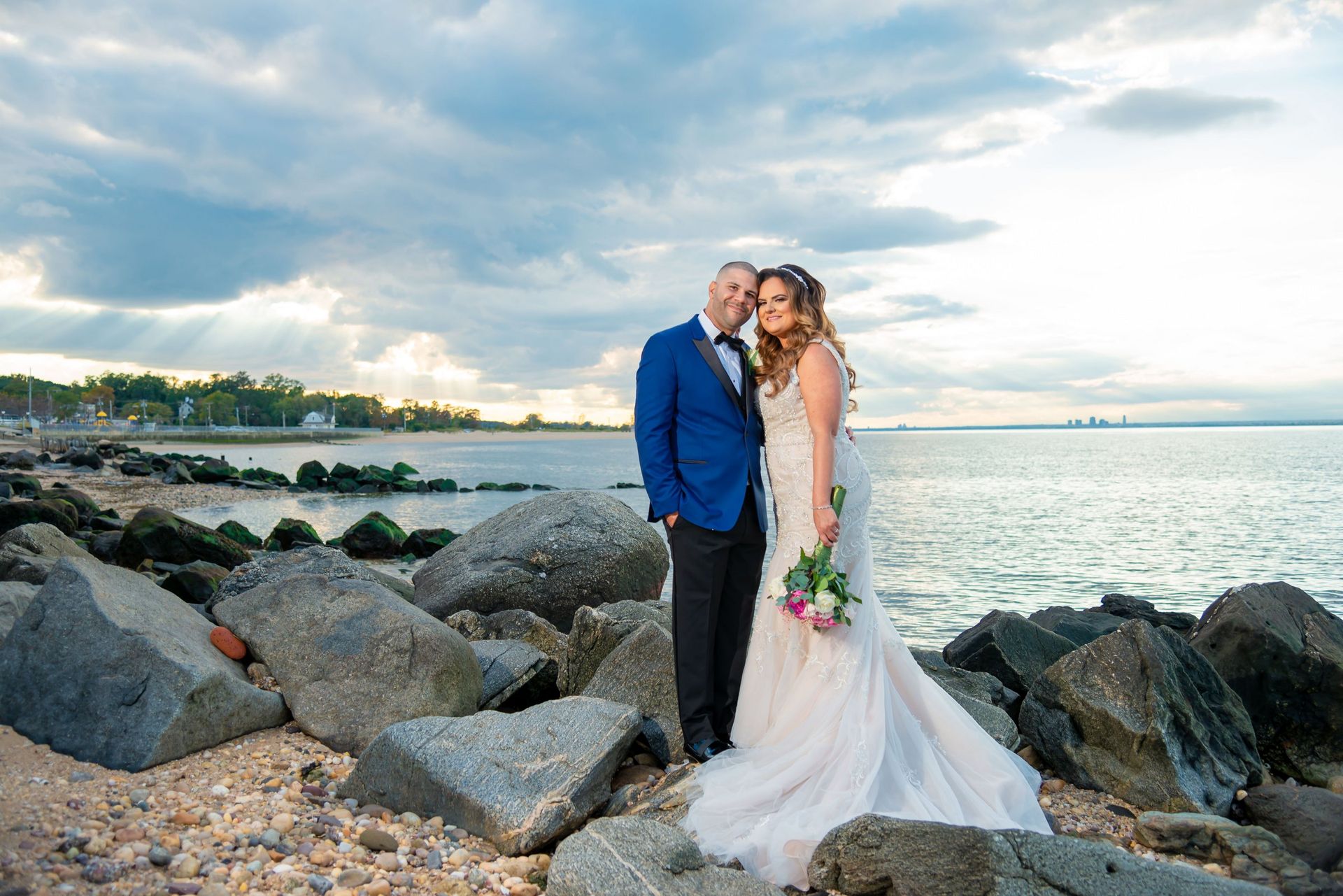 Bride and groom standing among rocks along a cloudy shoreline