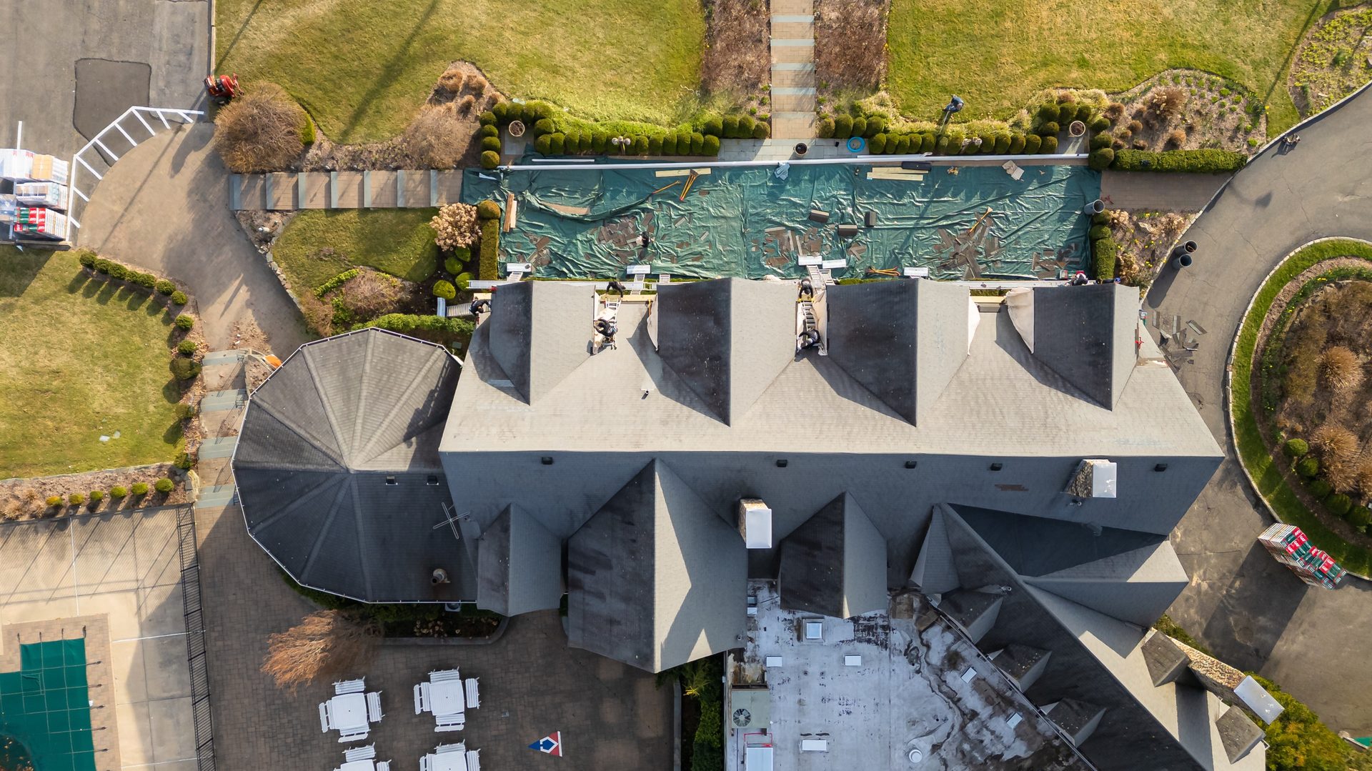 Roof replacement in progress — crew on ladders with the old roof stripped and protective tarps down