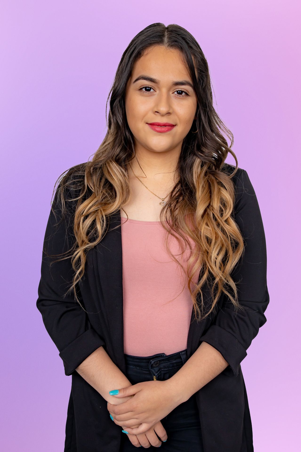 Young woman with long wavy highlighted hair in a black blazer and pink top on a purple background