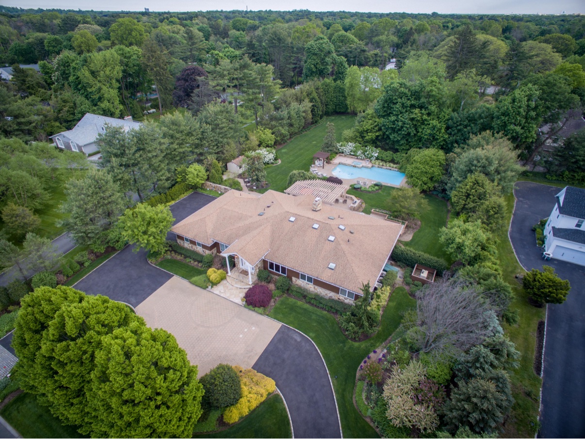 Aerial view of a ranch-style home with a pool, pergola and tree-lined circular driveway