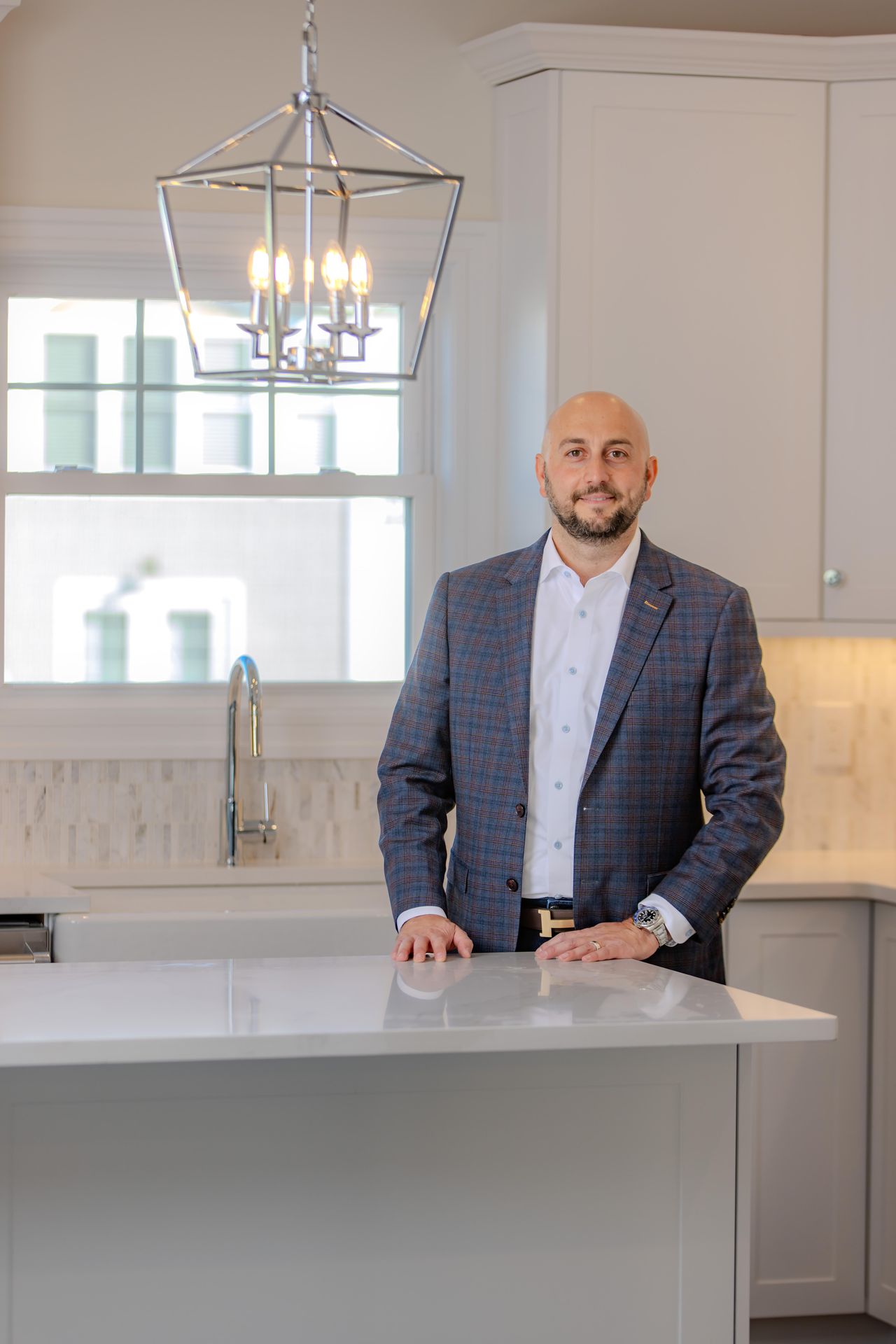 Bald man in a blue plaid blazer and white shirt standing at a white kitchen island