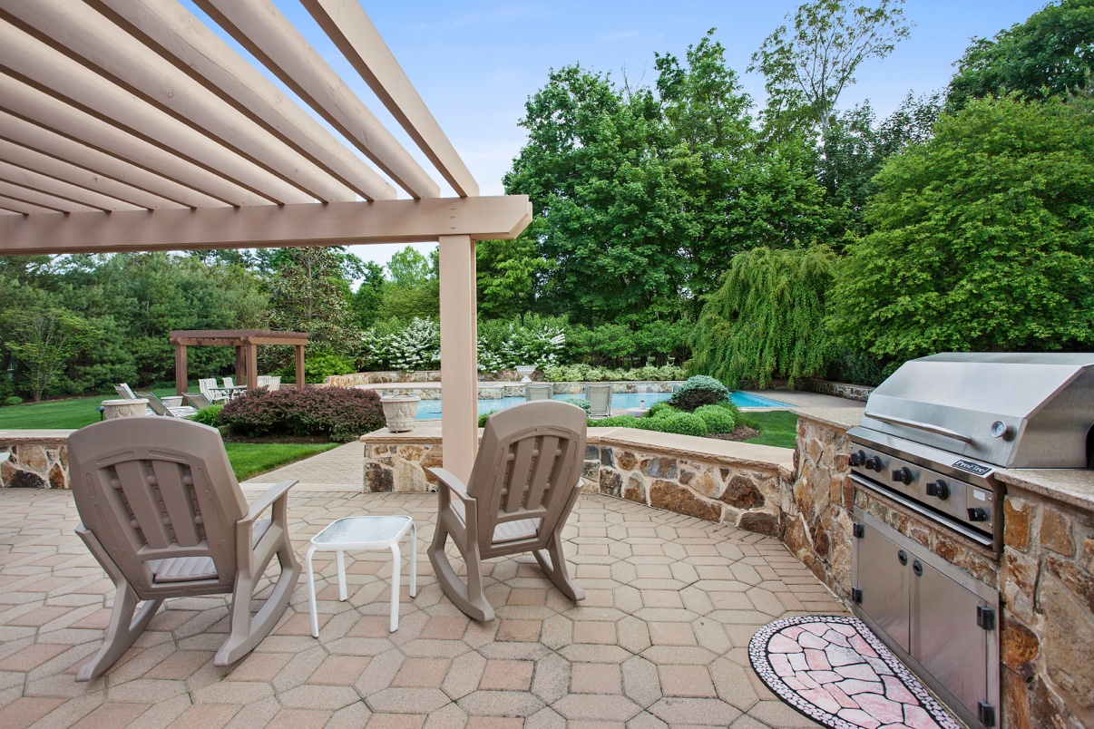 Backyard patio with a pergola, rocking chairs, a stone outdoor kitchen and a pool beyond