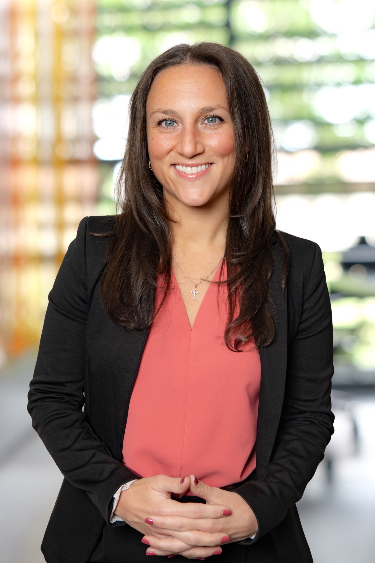 Smiling woman in a black blazer over a coral top by a glass wall