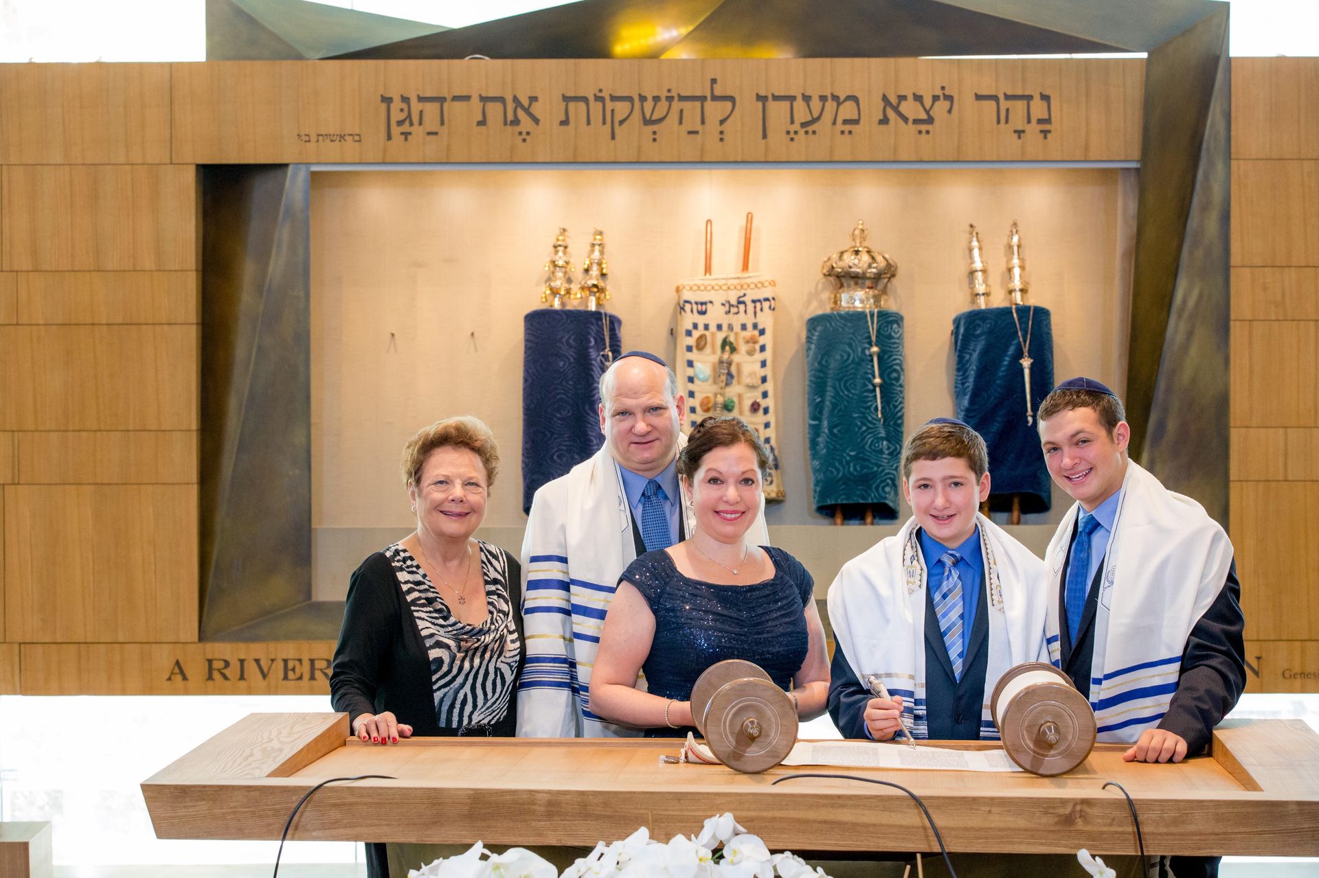 Bar mitzvah family gathered at the bimah with Torah scrolls in a wood-lined sanctuary