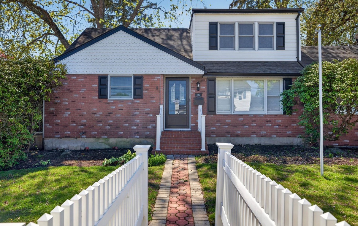 Front exterior of a brick and shingle home behind a white picket fence