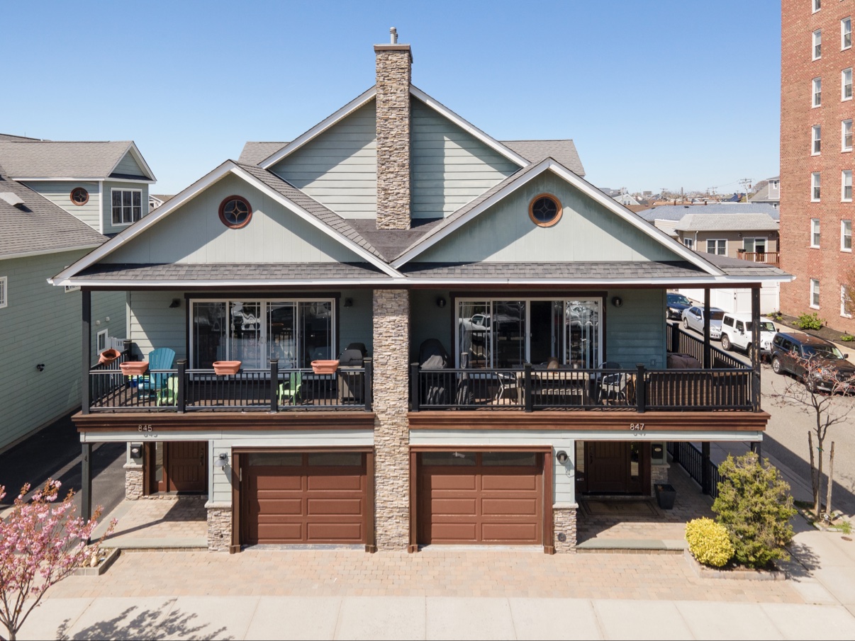 Front elevation of a teal two-unit townhouse with a stone chimney and ground-floor garages