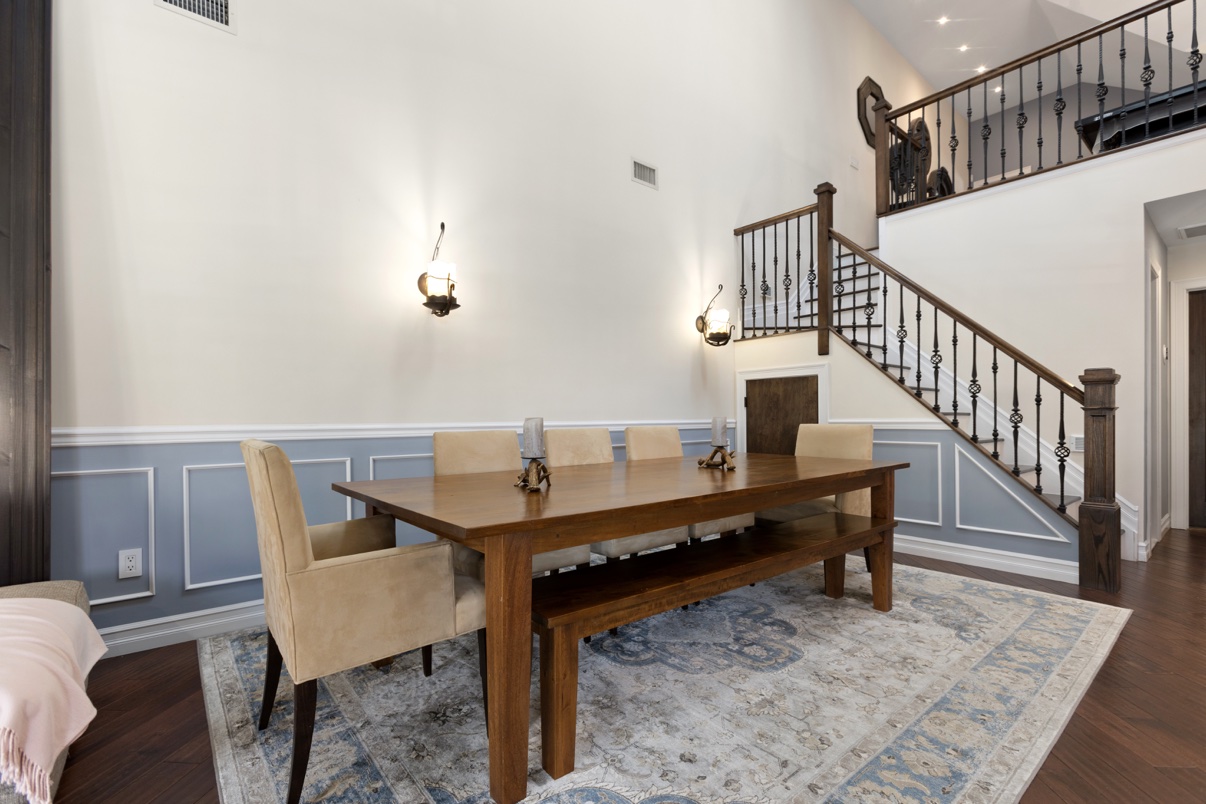 Dining room with a wooden table, upholstered chairs and a staircase with iron railings