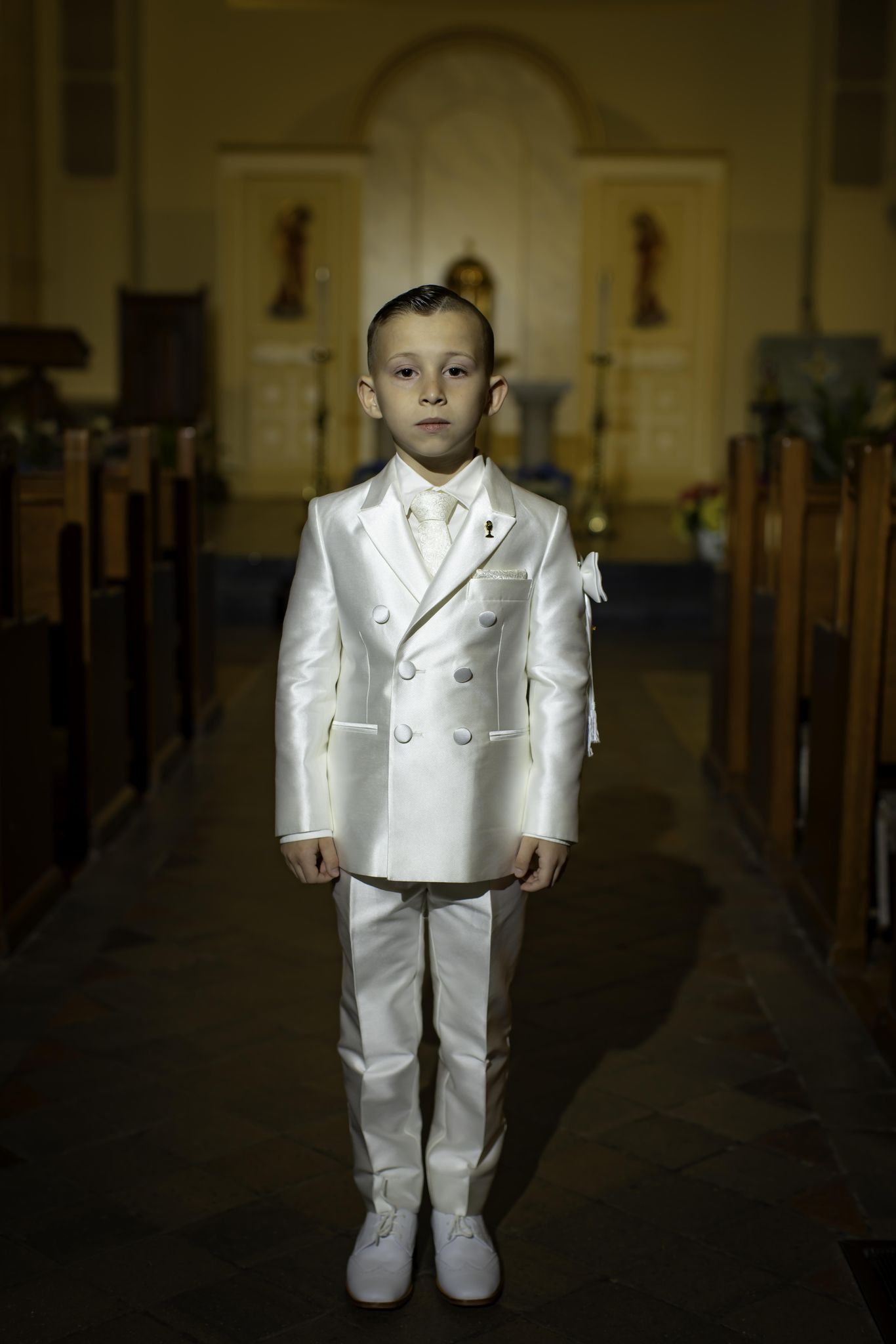 Boy in white communion suit in church aisle