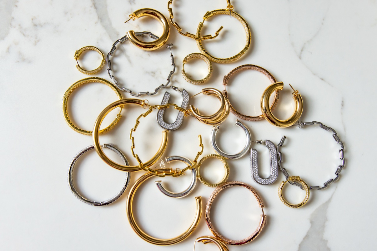Flat-lay of gold and silver hoop earrings and bangles on marble
