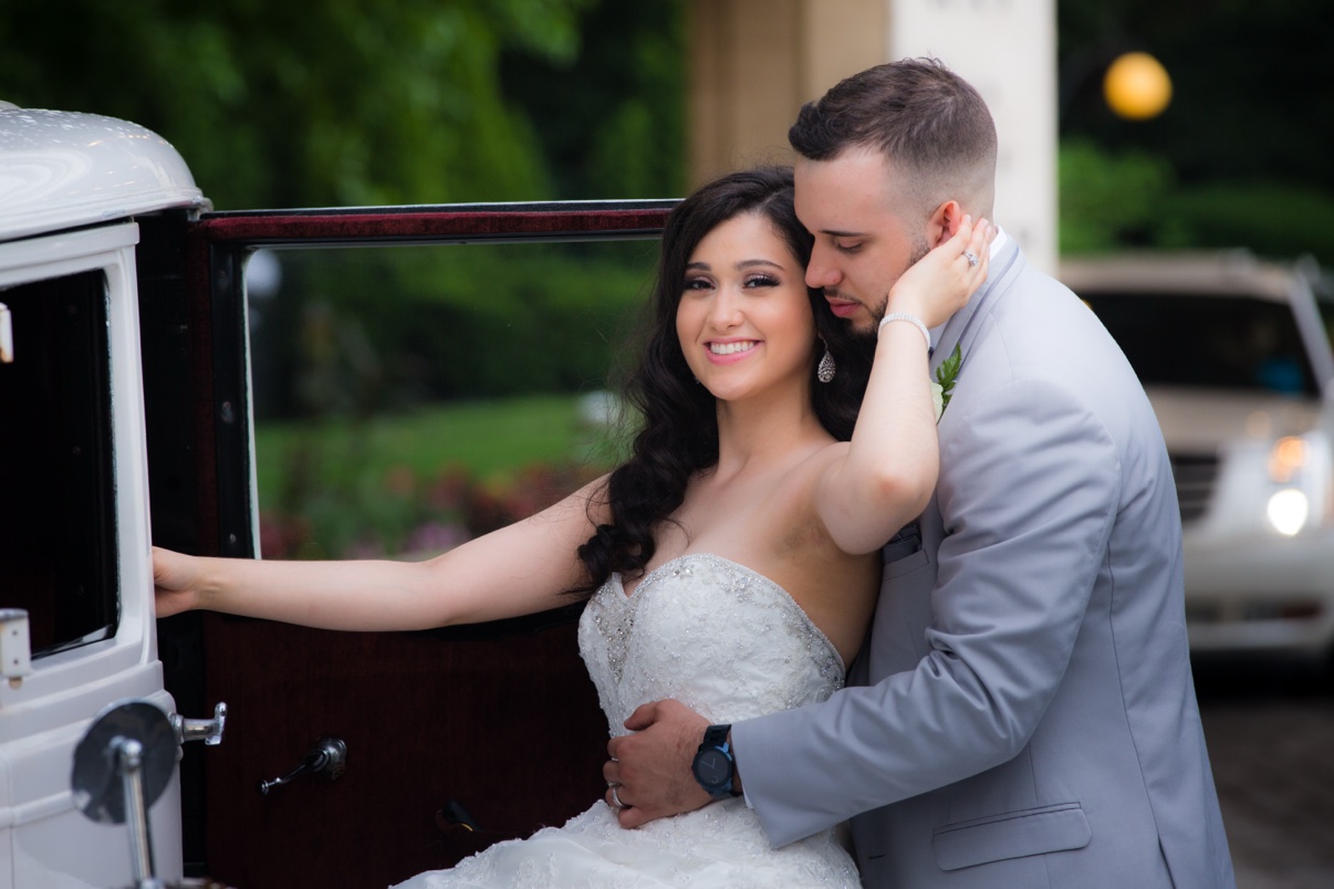 Bride and groom embracing beside a vintage car