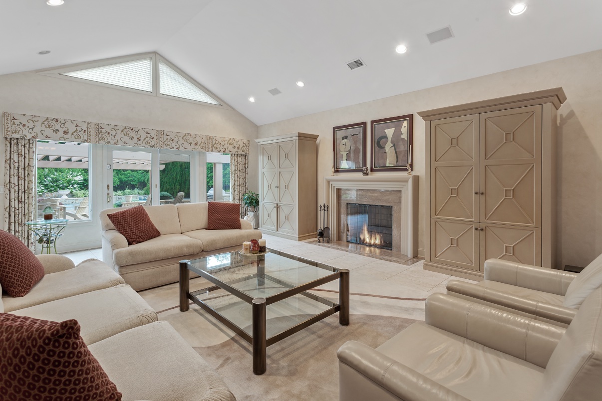 Living room with a lit fireplace, cream sofas, a glass coffee table and garden-view doors