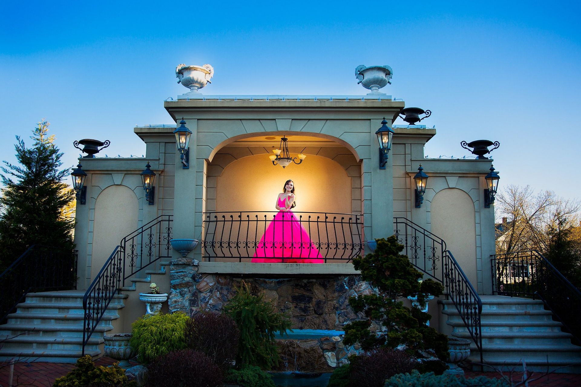 Sweet 16 celebrant in a vivid pink gown beneath an illuminated garden pavilion