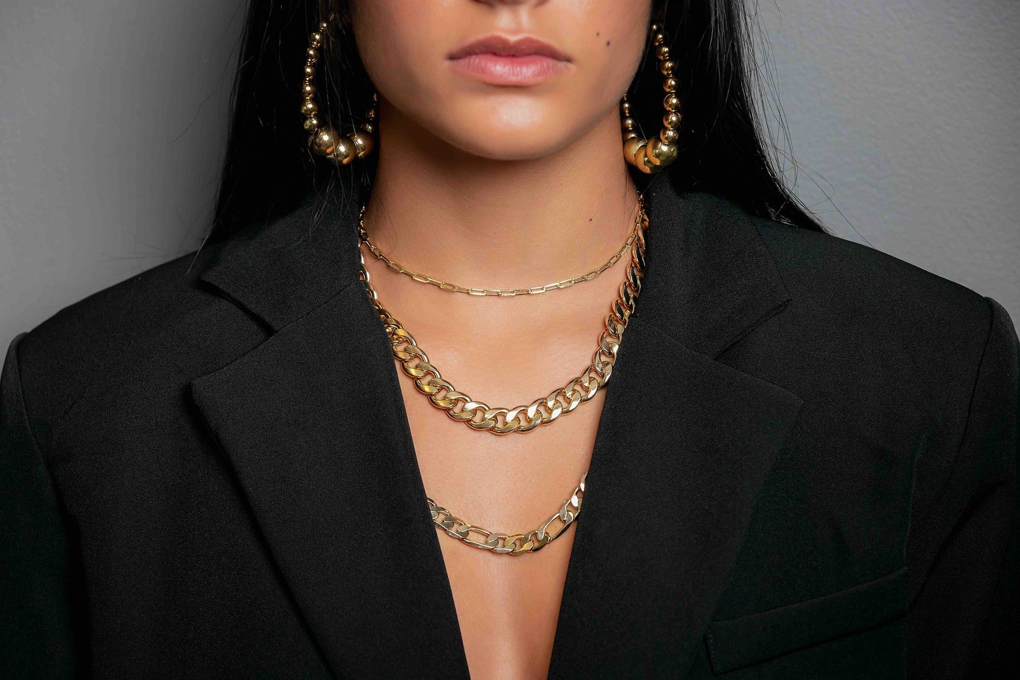 Model wearing layered gold necklaces with black blazer